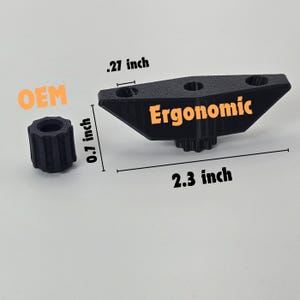 Könnte beinhalten: Schwarzer, 3D-gedruckter ergonomischer Knopf aus Kunststoff mit drei Löchern und einem sternförmigen Zahnrad. Der Knopf ist 2,3 Zoll lang und 0,27 Zoll breit. Der Knopf ist mit "Ergonomic" beschriftet. Ein kleinerer schwarzer Kunststoffknopf ist ebenfalls abgebildet und hat einen Durchmesser von 0,1 Zoll.