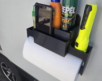 May include: Black plastic organizer with compartments for holding a phone, bug spray, sunscreen, and a flashlight. A roll of paper towels is attached to the side.