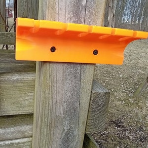 May include: Orange plastic wall-mounted storage rack with six slots for holding items. The rack is attached to a wooden post with two screws.