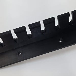 May include: A black, wall-mounted rack with seven curved slots, likely for holding items. The rack has a rectangular base with two holes for mounting. The design is simple and functional, suitable for organizing various items.