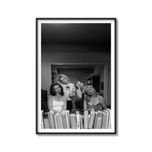 Puede incluir: Impresión enmarcada en blanco y negro que muestra a cuatro personas reunidas alrededor de una mesa con libros. Los sujetos miran a la cámara. La imagen es un retrato y la impresión está en un marco negro.