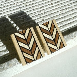 Op de afbeelding: Een paar houten oorbellen met een chevron-patroon in tinten bruin, wit en zwart.