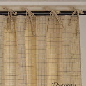 Könnte beinhalten: Ein Paar beigefarbene Vorhänge mit einem schwarz-weiß karierten Muster. Die Vorhänge haben einen gerafften oberen Teil und sind an einer schwarzen Gardinenstange aufgehängt.