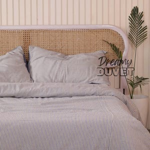 May include: A bed featuring a striped duvet cover and pillowcases in white and blue. The headboard is made of woven rattan. The text "Dreamy DUVET" is visible on the right side of the bed.
