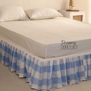 May include: A bed with a white fitted sheet and two white pillows. The bed skirt is blue and white checkered. The text "Dreamy DUVET" is printed on the fitted sheet.
