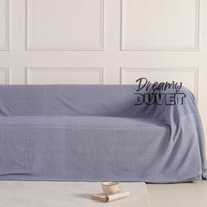May include: A blue and white striped sofa cover on a sofa. The cover features a horizontal stripe design. A white rug, a book, and a teacup are in front of the sofa. The text "Dreamy Duvet" is visible on the cover.