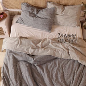 May include: A white and gray striped duvet cover with the text "Dreamy Duvet" on the bottom. The duvet cover is on a bed with two matching pillowcases.