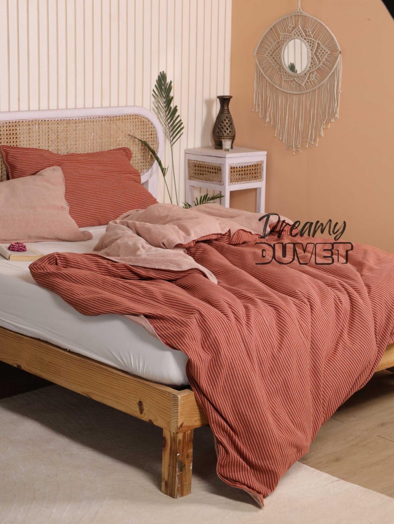 May include: A bed with a wooden frame and a woven headboard. The bedding features a red-orange striped duvet, matching pillowcases, and a light pink pillow. The text "Dreamy DUVET" is displayed on the duvet.