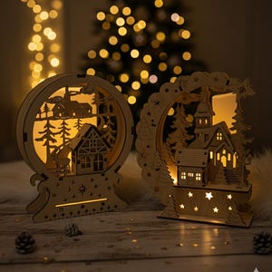 Puede incluir: Dos decoraciones de pueblo navide&ntilde;o de madera con c&aacute;lida iluminaci&oacute;n interior. Una es circular, la otra en forma de arco. Ambas presentan dise&ntilde;os recortados de casas, &aacute;rboles y estrellas. El fondo est&aacute; suavemente iluminado con un &aacute;rbol de Navidad y luces de hadas.