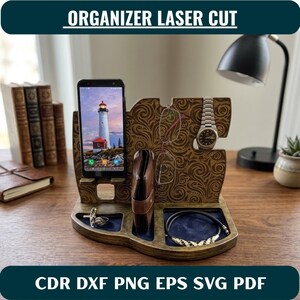 Może przedstawiać: Drewniany organizer na biurko z wycinanymi laserowo wzorami wirów. Zawiera podstawkę na smartfon, szczelinę na okulary, haczyk na zegarek na rękę oraz dwie wnęki wyłożone ciemnoniebieskim aksamitem do przechowywania drobnych przedmiotów.