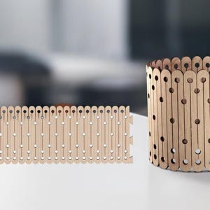May include: A wooden cylindrical container and a flat wooden panel, both with a repeating pattern of vertical slats and circular cutouts. The objects are light brown and sit on a white surface.