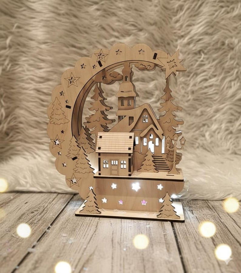 Puede incluir: Una escena de pueblo navide&ntilde;o de madera con una iglesia, casas y &aacute;rboles. La escena est&aacute; iluminada con peque&ntilde;as luces, y una forma de estrella recortada est&aacute; en la parte superior. La estructura de madera est&aacute; sobre una base de madera.