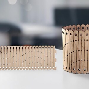 May include: Two wooden decorative items. One is a rectangular panel with a wavy design, and the other is a cylindrical container. Both are made of light-colored wood with a series of cut-out shapes.