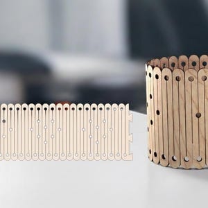 May include: A wooden cylindrical container and a flat wooden piece. The container is made of vertical wooden slats with evenly spaced holes. The flat piece has a similar design, with vertical slats and holes, and is designed to interlock with the container.