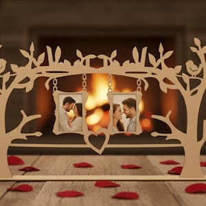 May include: A wooden photo frame in the shape of a tree, with two hanging picture frames. The frame has a heart-shaped cutout and is decorated with leaves and birds. Red rose petals are scattered on the table.