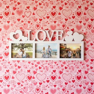 May include: A white "LOVE" photo frame with three openings, set against a pink wallpaper covered in red hearts. The frame holds three photos of couples. The wallpaper has various heart designs and the words "Alive" and "Love".
