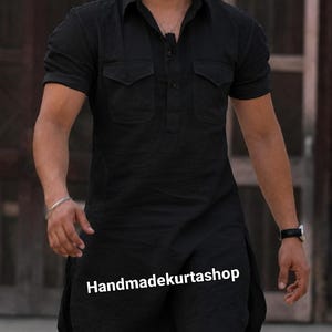 Könnte beinhalten: Ein schwarzes Kurzarmhemd mit klassischem Kragen, einer kurzen Knopfleiste und zwei Brusttaschen mit Klappen. Das Hemd hat einen langen, geraden Saum mit Seitenschlitzen. Der Text "Handmadekurtashop" ist auf der Vorderseite aufgedruckt.