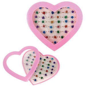 May include: A pink heart-shaped box filled with colourful rings. The box is open and the rings are visible. The rings are made of silver and have colourful stones.