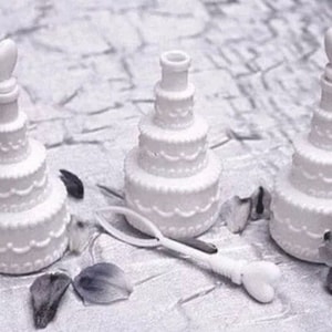 May include: Three white plastic wedding cake shaped bubble blowers with heart shaped tops.