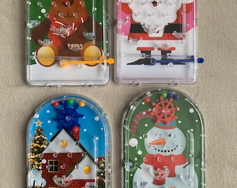 May include: Four Christmas-themed handheld water ring toss games. Each game features a different holiday character: a reindeer, Santa Claus, a house with a Christmas tree, and a snowman. The games have colored buttons and are filled with water and small rings.