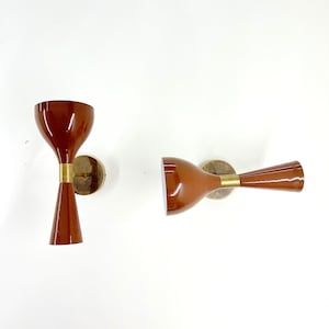 Könnte beinhalten: Zwei braune Wandleuchten mit goldenen Akzenten. Die Leuchten haben die Form einer Trompete und ein modernes Design.