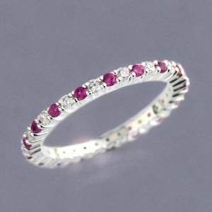 May include: A thin silver-toned band ring featuring an alternating pattern of round, vibrant pink rubies and clear, sparkling white diamonds set along the entire circumference of the metal band, creating a continuous, symmetrical, and elegant design.