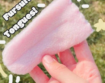 May include: A pink furry tongue for a fursuit. The tongue is made of soft, plush fabric and is held in a hand.