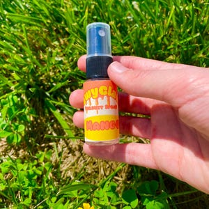 May include: A small clear plastic bottle with a black spray nozzle. The bottle has a yellow and orange label with the text "Juicy Glam" and "Mango" on it.