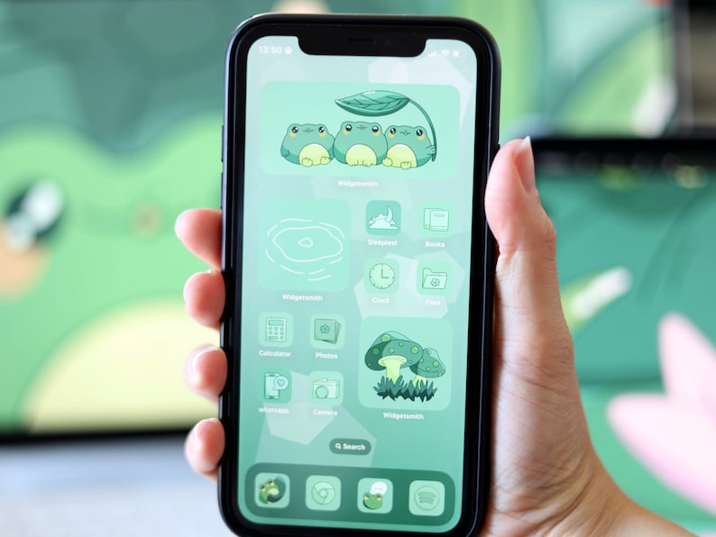 May include: A green and white phone screen with a custom home screen design. The design features frogs, mushrooms, and a pond. The apps are labeled with text such as "Calculator", "Photos", "Clock", and "Files".