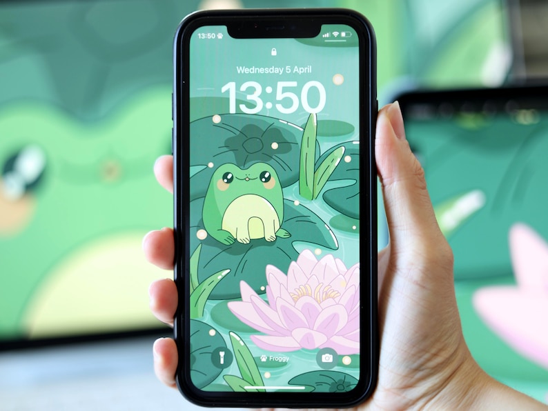 May include: A green frog with big eyes sits on a lily pad in a pond. The background is a green and white pattern of lily pads and water. The phone screen shows the time as 13:50 and the date as Wednesday 5 April.