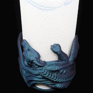 Könnte beinhalten: Ein blaugrüner Drachen-förmiger Papierhandtuchhalter. Der Drache ist um die Papierhandtuchrolle gewickelt.