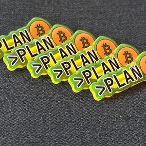 Może przedstawiać: Sześć zielono-żółtych przypinek z napisem "PLAN" i symbolem Bitcoina. Słowo "PLAN" jest czarne, z białym obrysem. Symbol Bitcoina jest pomarańczowy z białym "B".