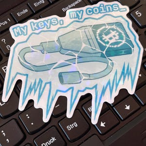 May include: A holographic sticker with the text "My keys, my coins" in a light blue font. The sticker features a stylized illustration of a key and a wallet, with a digital currency symbol. The sticker has a jagged, icy border.