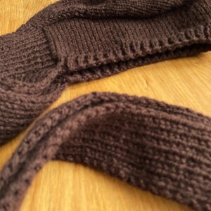 A dark brown knittedbalabonnet. The hat is a beanie style with a folded brim. The scarf is a long, rectangular shape. Both items are made of a thick, textured yarn, perfect for cold weather.