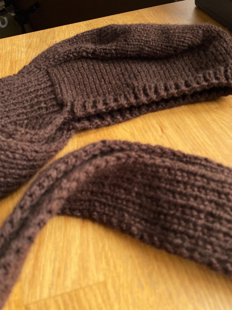 A dark brown knittedbalabonnet. The hat is a beanie style with a folded brim. The scarf is a long, rectangular shape. Both items are made of a thick, textured yarn, perfect for cold weather.