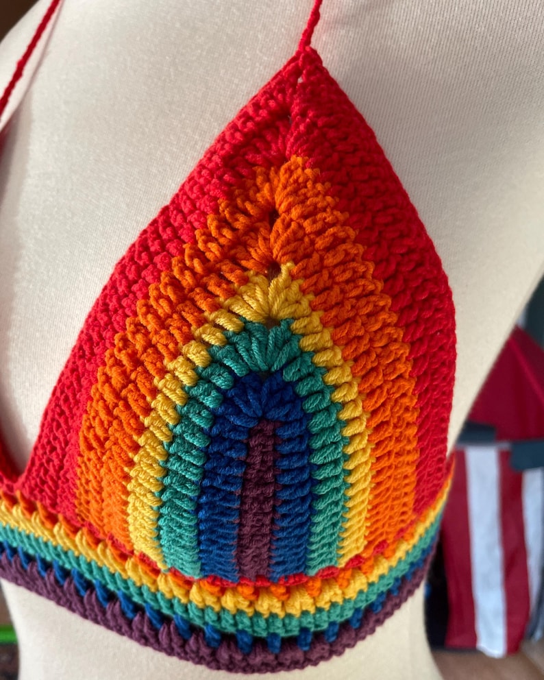 A close-up shot of a handmade crochet bikini top featuring the colors of the Pride flag.
