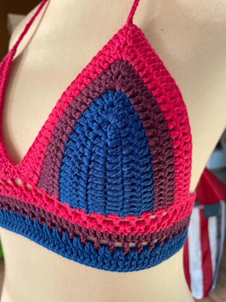 A close-up shot of a handmade crochet bikini top featuring the colors of the bisexual Pride flag.