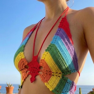 Pode incluir: Top de crochê feito à mão em um esquema de cores do arco-íris. O top apresenta um design de pescoço halter com alças vermelhas e um detalhe central de crochê vermelho. O padrão do arco-íris inclui listras vermelhas, laranja, amarelo, verde, azul e roxo.