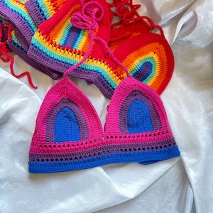 A rainbow crochet top with a pink, blue, purple, and yellow color scheme. The top is made with a crocheted stitch and has a triangle shape.
