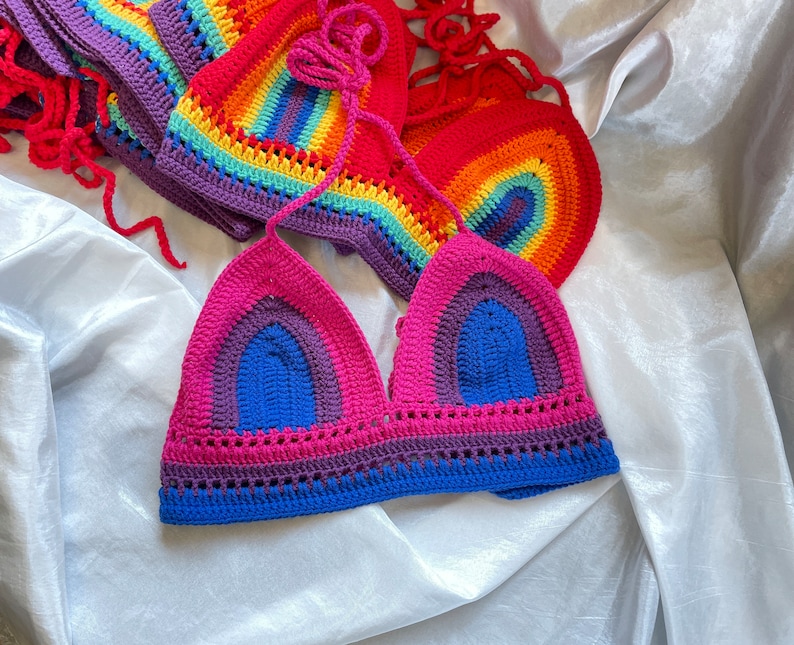A rainbow crochet top with a pink, blue, purple, and yellow color scheme. The top is made with a crocheted stitch and has a triangle shape.