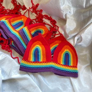 A stack of rainbow crochet tops with purple trim. The tops are made with a colorful yarn that resembles a rainbow.
