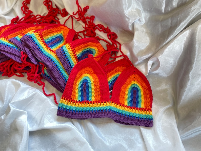 A stack of rainbow crochet tops with purple trim. The tops are made with a colorful yarn that resembles a rainbow.