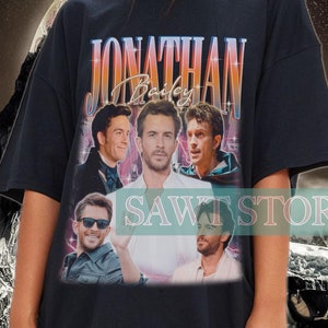May include: Black oversized t-shirt featuring a vintage-style graphic of Jonathan Bailey. The design includes multiple images of the actor and the text "Jonathan Bailey" in a retro font. The shirt is worn by a person.