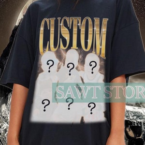 May include: Black oversized t-shirt with the word "CUSTOM" in gold lettering and a graphic of four figures with question marks for faces. The t-shirt is worn by a person with long dark hair and is styled with black leather pants.