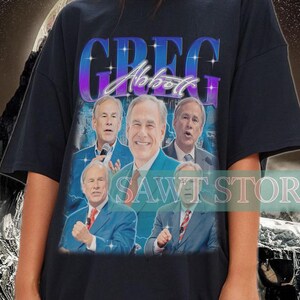 Puede incluir: Camiseta negra con un gráfico de Greg Abbott y su nombre en degradado. La camiseta tiene un diseño vintage con múltiples imágenes de la persona. El texto "SAWT STORE" es visible en la camiseta.