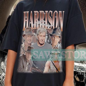 May include: Black oversized t-shirt with a vintage-style graphic print of Harrison Ford and other actors from the Indiana Jones franchise. The print features the text "HARRISON FORD" in a gold font.