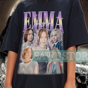May include: Black oversized t-shirt featuring a graphic print of a group of women with the text "EMMA" in a purple and yellow gradient. The graphic is set against a background of lightning bolts.