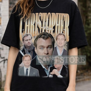 Könnte beinhalten: Ein schwarzes Kurzarm-T-Shirt mit einem großen Grafikdruck von Christopher Nolan. Das Design zeigt den Namen Christopher Nolan in goldener Schrift oben und fünf verschiedene fotografische Porträts des Regisseurs darunter.
