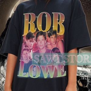 May include: Black oversized t-shirt featuring a vintage-style graphic of Rob Lowe. The graphic includes a collage of photos of Rob Lowe and the text "ROB LOWE" in a colourful, retro font.