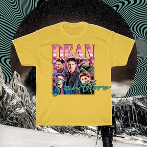 May include: Yellow t-shirt with a retro-style graphic of Dean Winchester from the TV show Supernatural. The graphic features a collage of Dean's face and other characters from the show. The text "Dean Winchester" is in pink and the text "Sawstore" is in green.